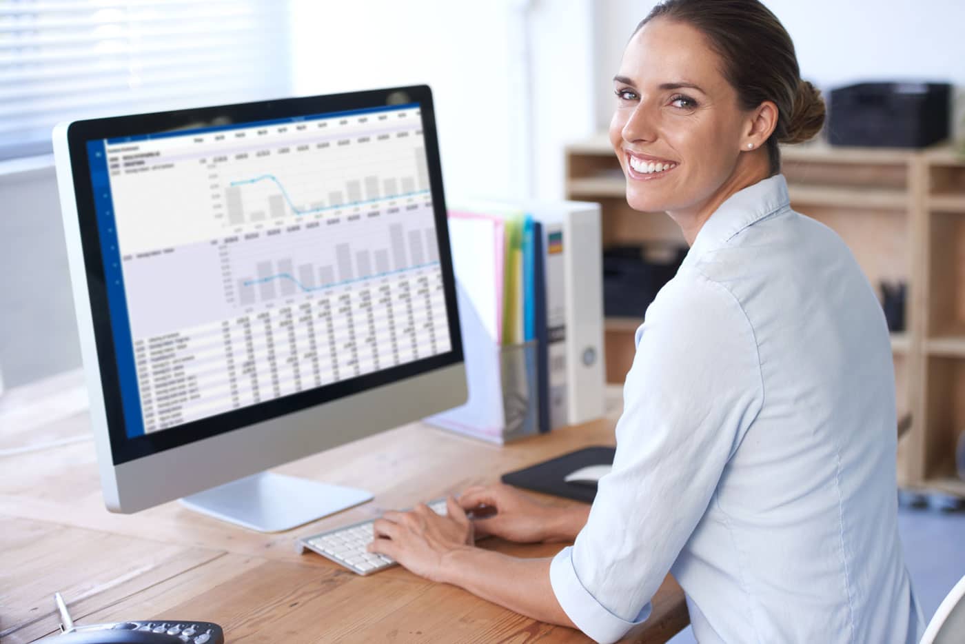 Smilende kvinde arbejder ved computer med grafer og data på skærmen.