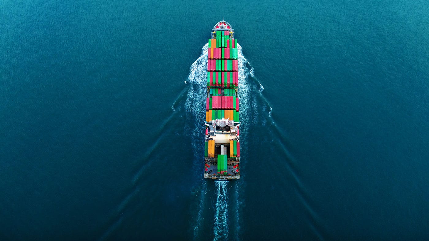et stort fragtskib fyldt med containere der sejer i havet, set fra oven